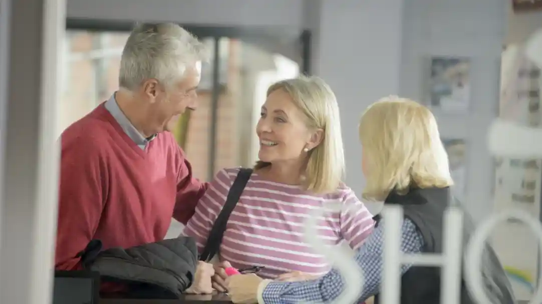 An older couple speaking to a lady on reception. Everyone is smiling and looking happy.