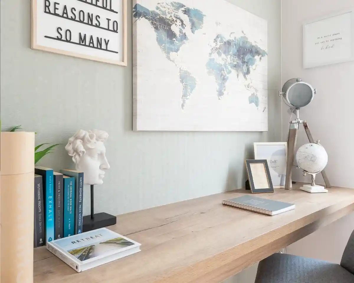 A modern workspace featuring a wooden desk with books, a small globe, a framed quote, and a decorative bust. A world map hangs on the wall, complementing the serene color palette of the room.