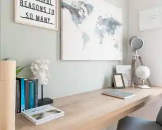 A modern workspace featuring a wooden desk with books, a small globe, a framed quote, and a decorative bust. A world map hangs on the wall, complementing the serene color palette of the room.