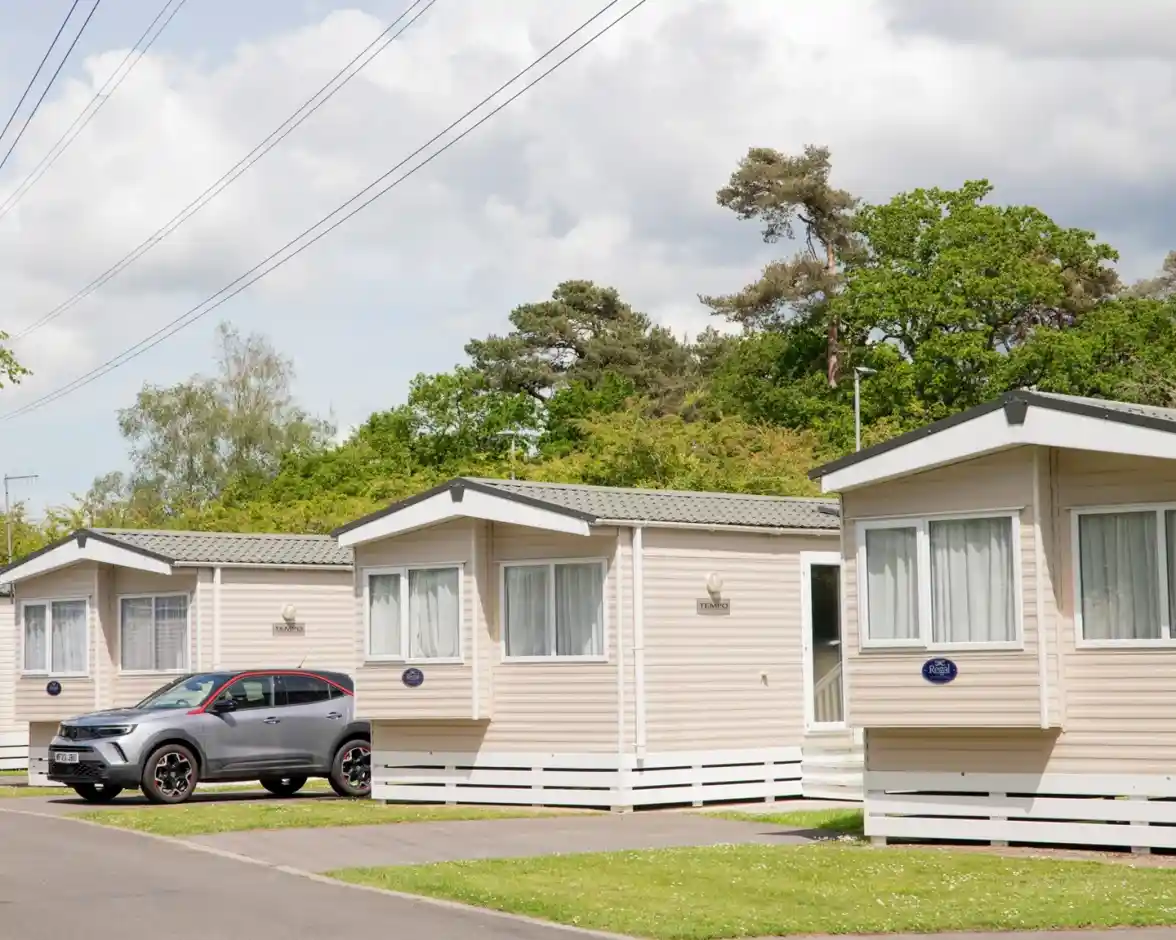 Row of modern static holiday homes with a parked car outside, surrounded by trees at Forest Edge Holiday Park