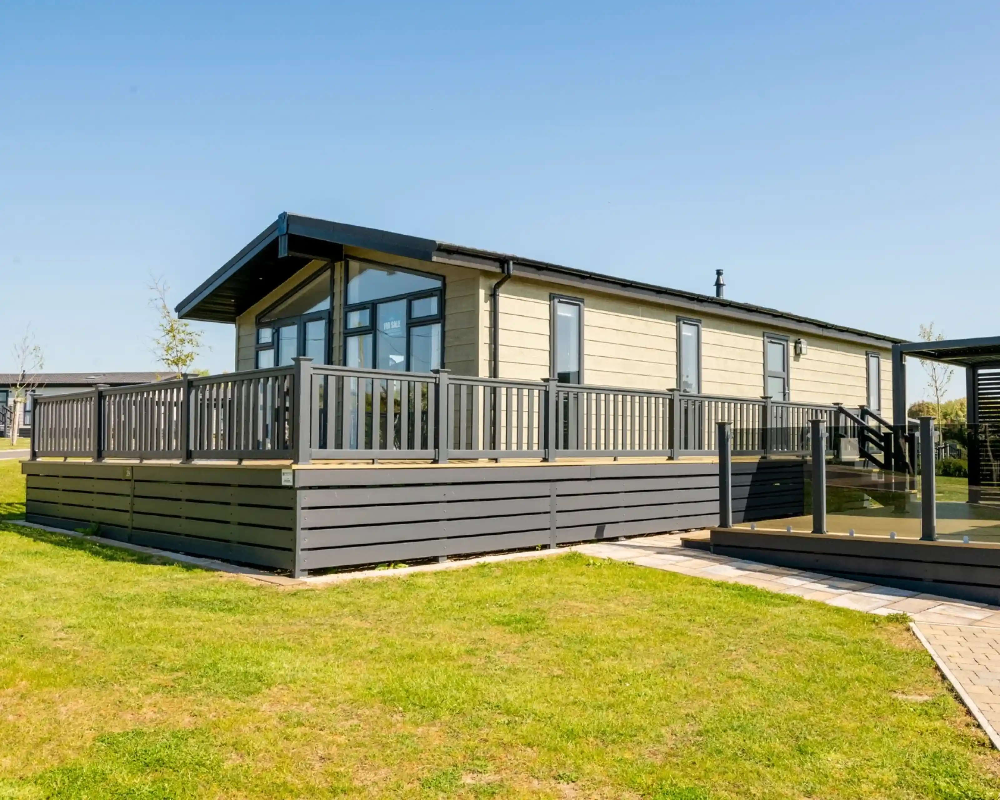 A modern, single-story modular home with a large deck, surrounded by lush green grass under a clear blue sky.