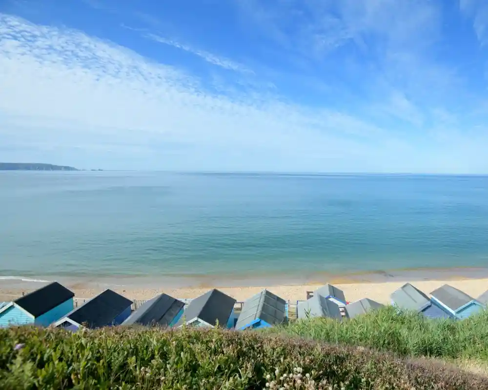 View of colorful beach huts on a sandy beach, with a clear blue sky and calm sea in the background.