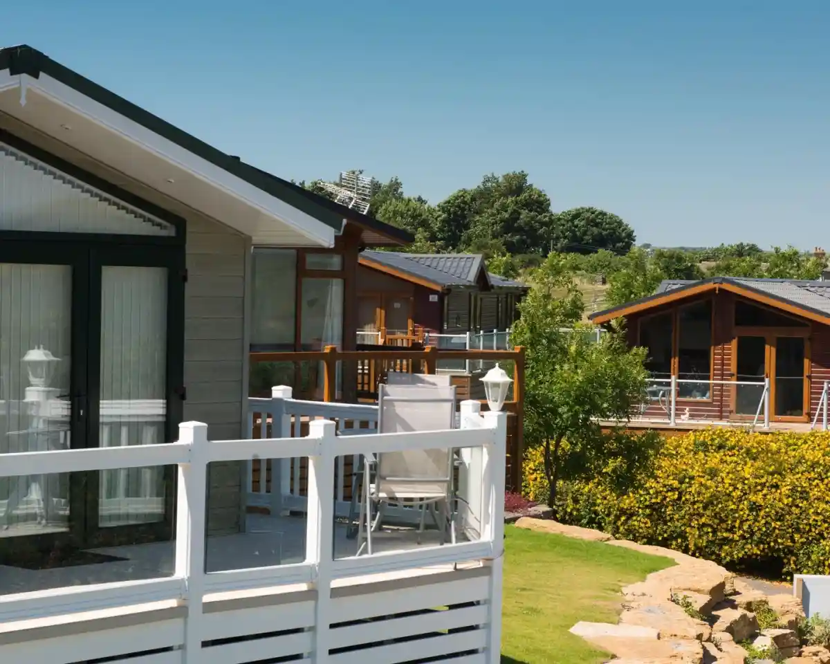 A row of modern vacation cabins set amidst greenery and landscaped gardens. Each cabin features balconies and large windows, with a clear blue sky above. Lush yellow flowering bushes and trees enhance the serene outdoor environment.