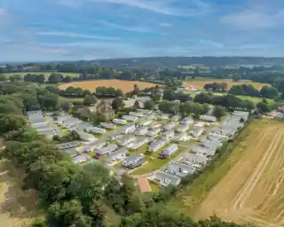 Aerial view of a mobile home park featuring neatly arranged homes surrounded by green trees and fields under a blue sky.