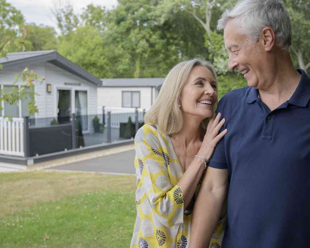 A senior couple poses in front of their mobile home, showcasing a warm and cheerful moment together.