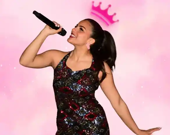 A young woman in a colorful, sequined dress sings joyfully into a microphone. She has a ponytail and is smiling, with a pink crown graphic above her head against a soft pink background.