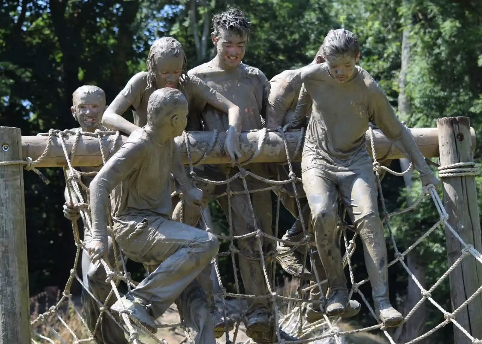 A vibrant inflatable water park is set up on a lake, with people actively engaging in various activities on the structures. In the background, a rocky hill topped with ruins is visible, surrounded by lush greenery under a clear blue sky.