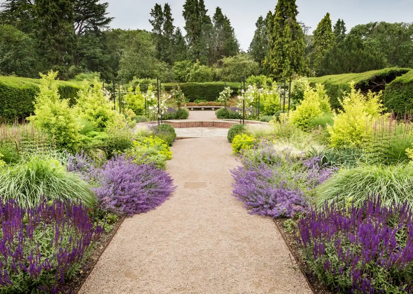 A serene garden scene with vibrant red and orange foliage surrounding a small stream. The water reflects the colorful leaves, while sunlight filters through the trees, creating a peaceful atmosphere.