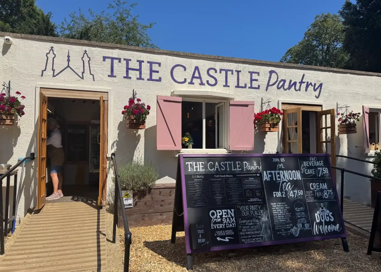Highcliffe Castle with intricate architecture and large windows, set against a bright blue sky and green lawns. The castle features towers and is surrounded by trees.