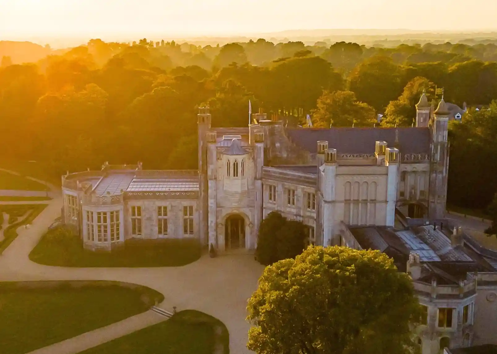 Highcliffe Castle with intricate architecture and large windows, set against a bright blue sky and green lawns. The castle features towers and is surrounded by trees.