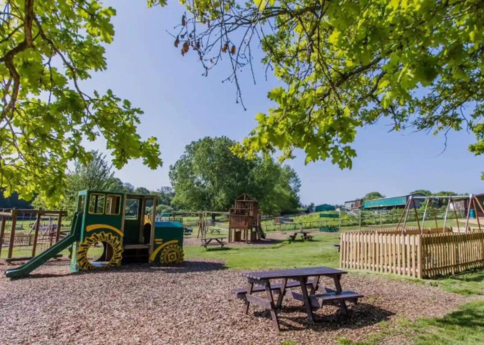 A smiling child with blonde hair holds a small, sleepy goat in her arms, both looking content. She is wearing a red sweatshirt, and a wooden fence is visible in the background.