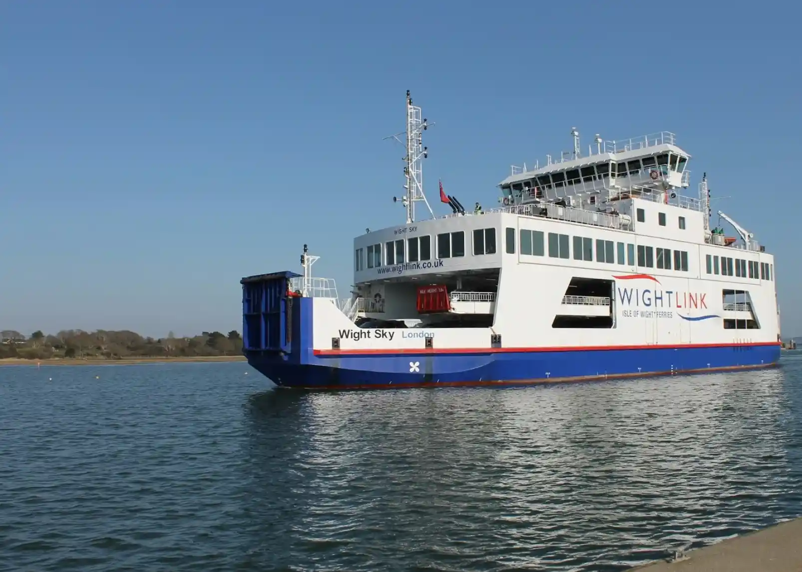 A quaint street lined with charming buildings, adorned with red, white, and blue bunting. Cobblestone path leads to a slightly elevated area with a tower in the distance.