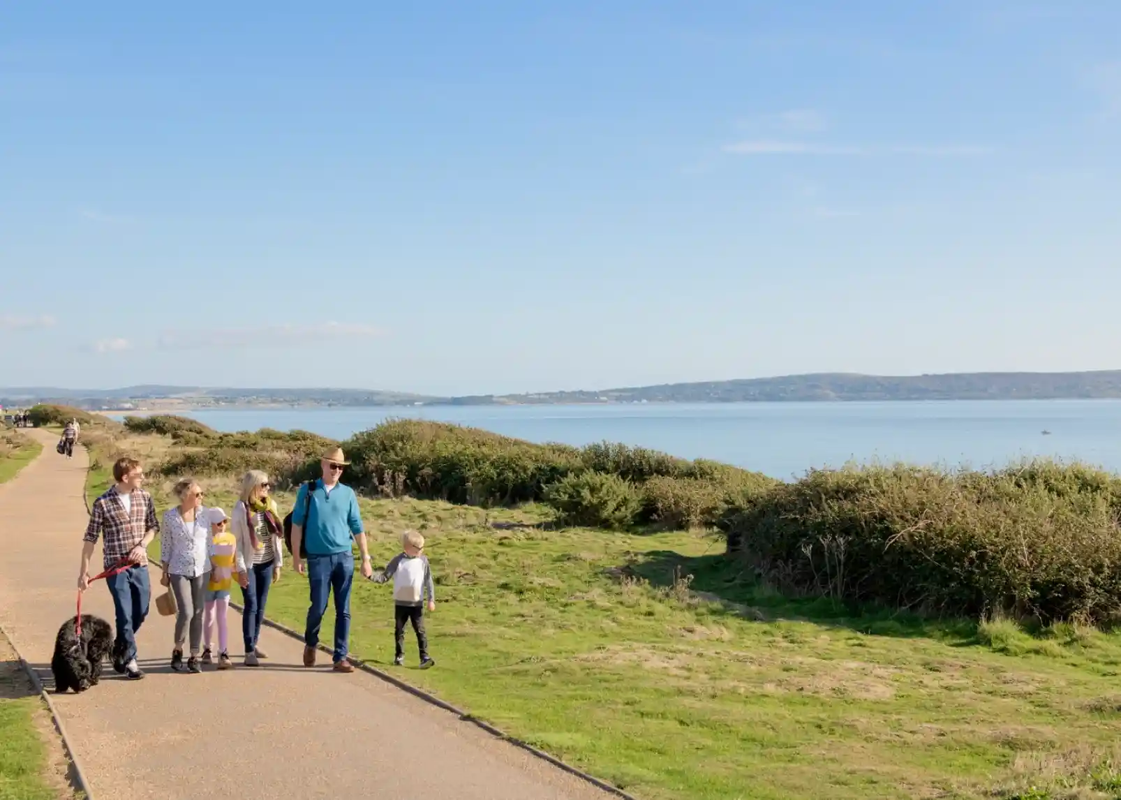 A vintage-style direction signpost with multiple arrows indicating distances to various locations: New Milton (3 miles), Christchurch (9.1 miles), Lymington (3.5 miles), Southampton (2.5 miles), and Keyhaven (1 mile). A thatched roof structure is visible in the background against a clear blue sky.