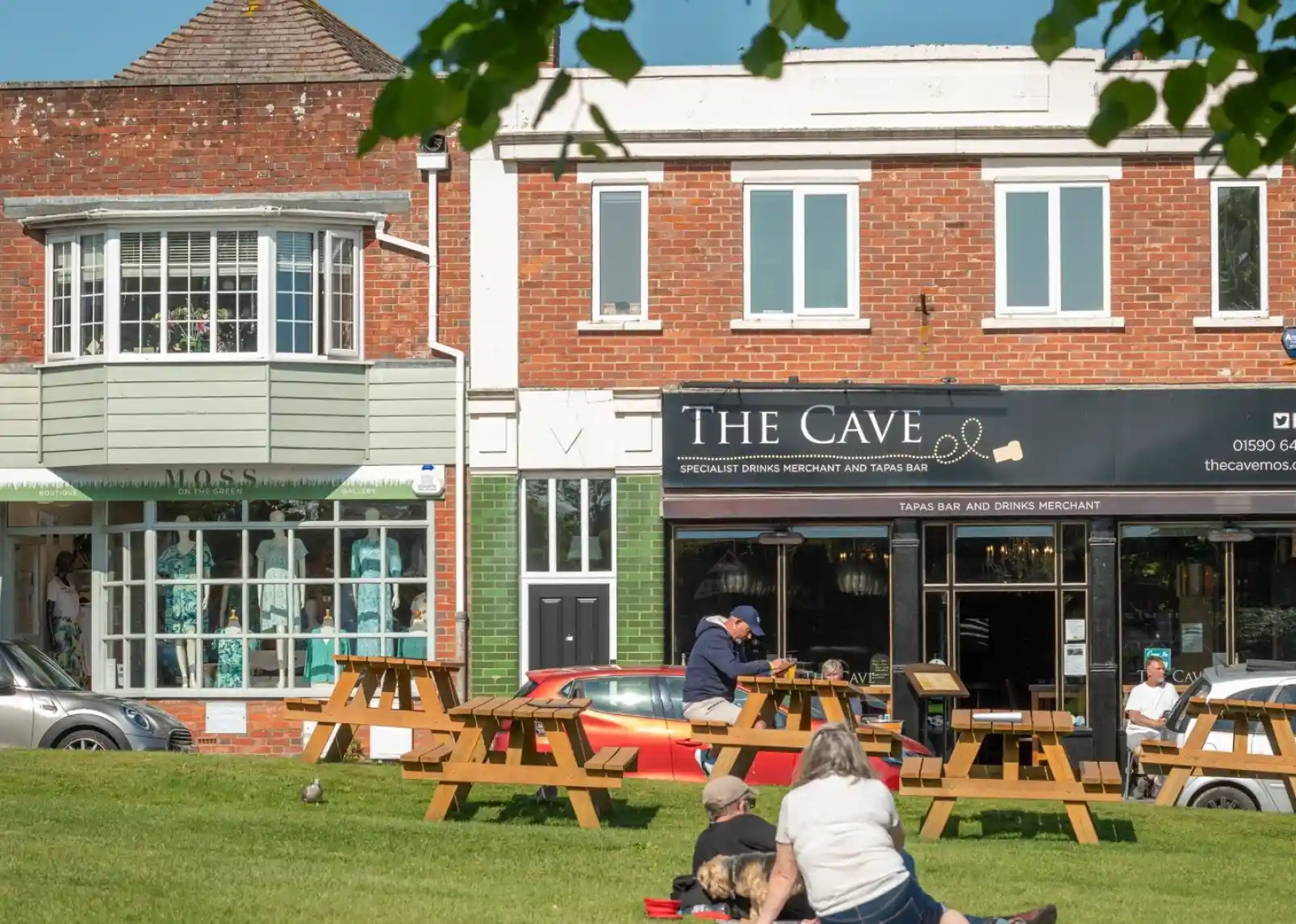 A vintage-style direction signpost with multiple arrows indicating distances to various locations: New Milton (3 miles), Christchurch (9.1 miles), Lymington (3.5 miles), Southampton (2.5 miles), and Keyhaven (1 mile). A thatched roof structure is visible in the background against a clear blue sky.