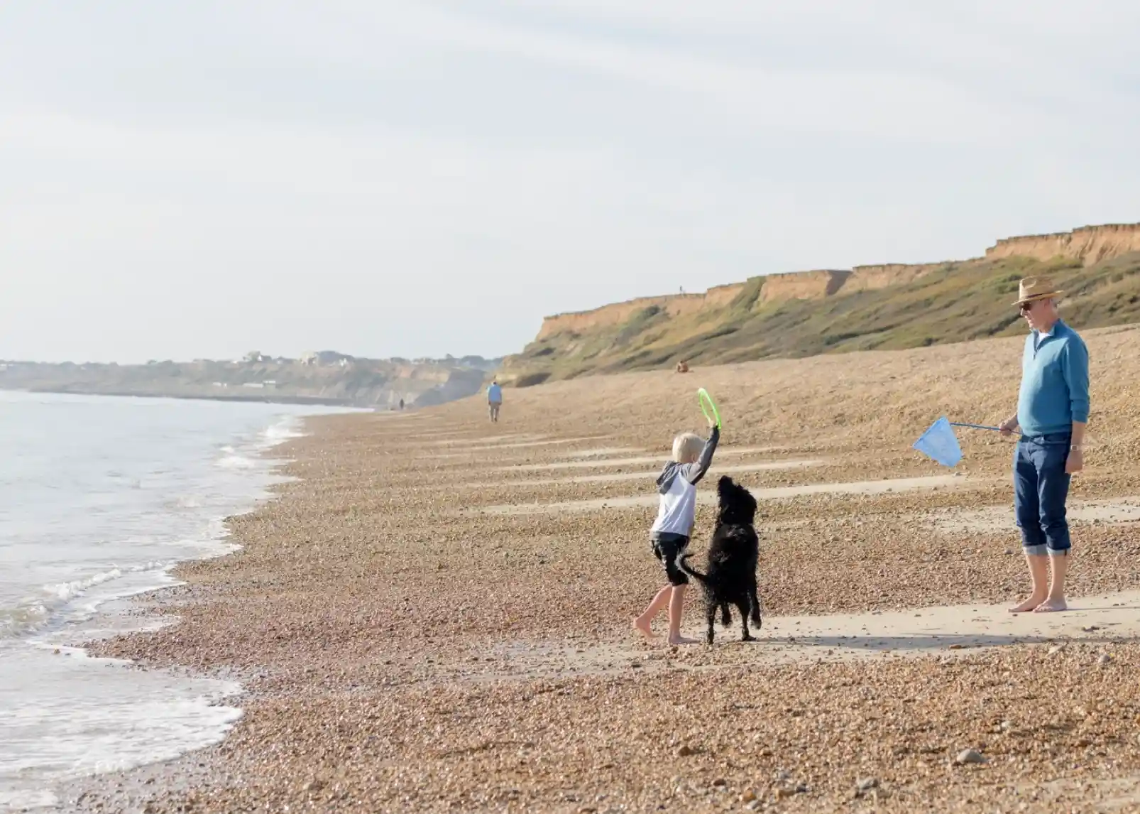 A vintage-style direction signpost with multiple arrows indicating distances to various locations: New Milton (3 miles), Christchurch (9.1 miles), Lymington (3.5 miles), Southampton (2.5 miles), and Keyhaven (1 mile). A thatched roof structure is visible in the background against a clear blue sky.