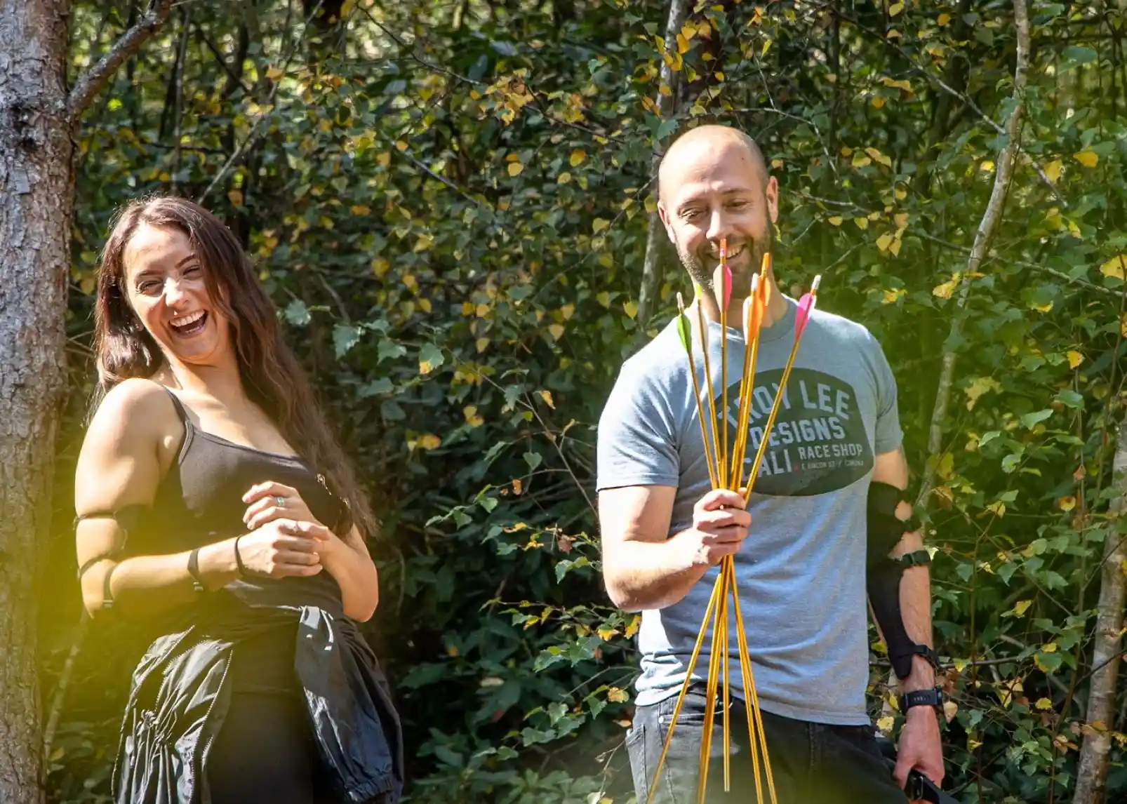 A family enjoys a sunny day canoeing on a calm river. Two adults and two children wear life jackets and are smiling while paddling. Lush greenery and reeds line the riverbank in the background.