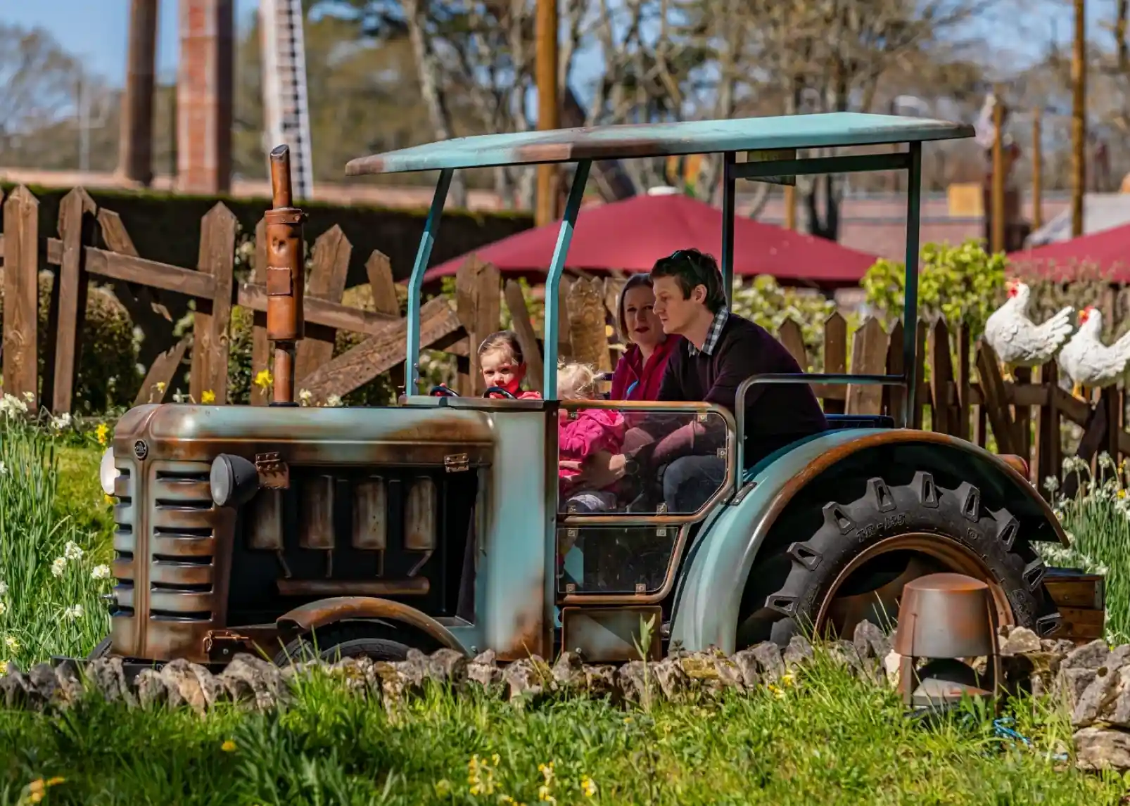A roller coaster with vintage-style cars zooms through a loop under a clear blue sky. Riders are enjoying the thrill, with some raising their arms in excitement. The track is a bright yellow, contrasting with the surrounding landscape.