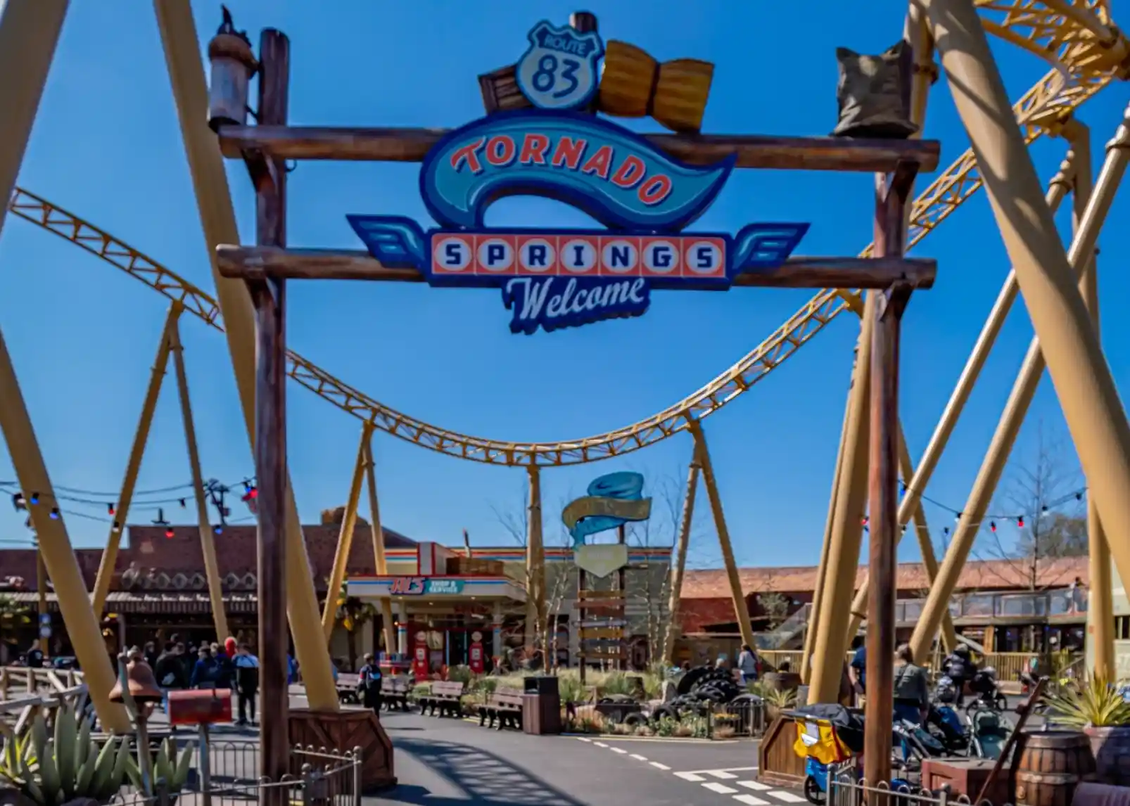 A roller coaster with vintage-style cars zooms through a loop under a clear blue sky. Riders are enjoying the thrill, with some raising their arms in excitement. The track is a bright yellow, contrasting with the surrounding landscape.