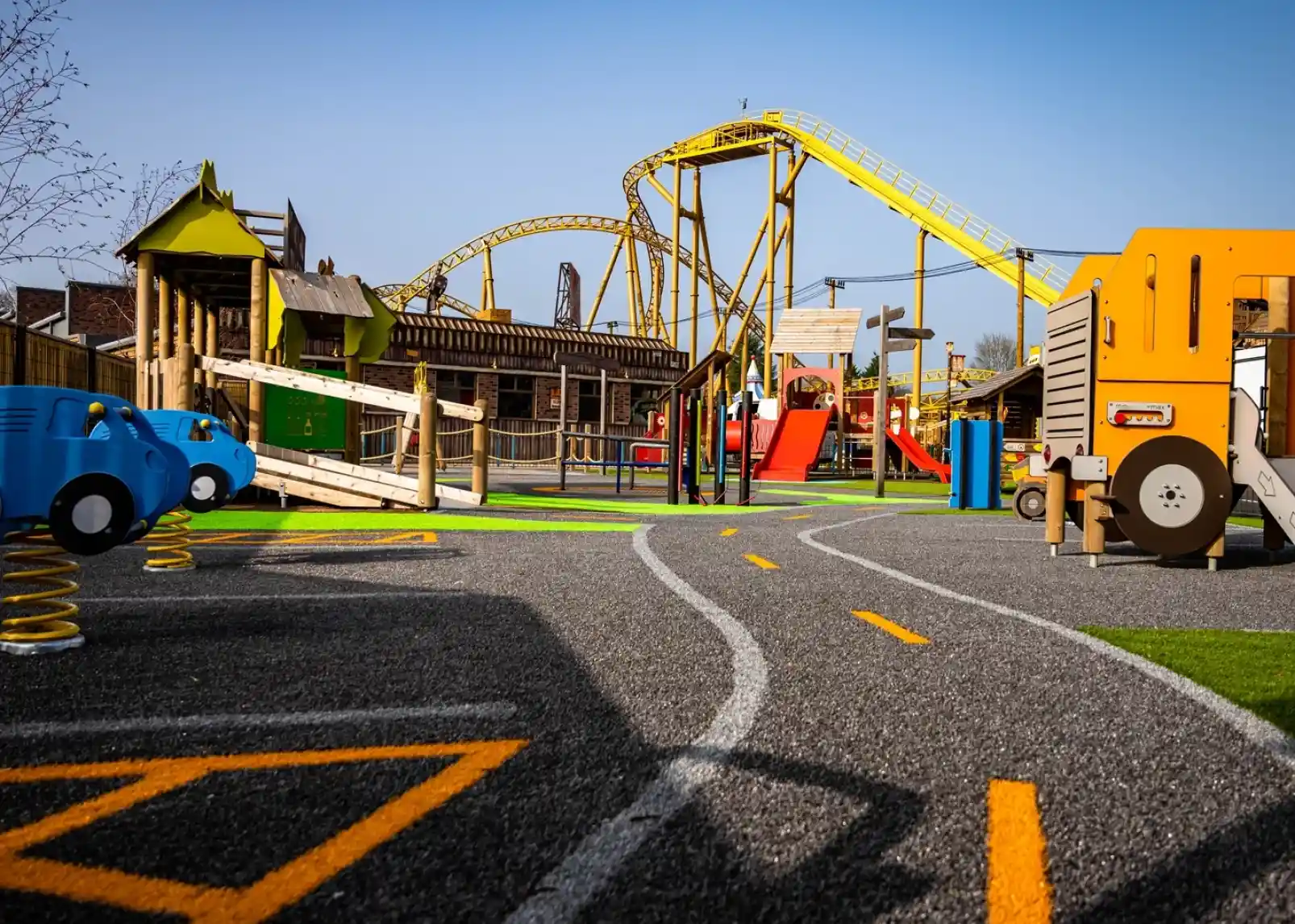 A roller coaster with vintage-style cars zooms through a loop under a clear blue sky. Riders are enjoying the thrill, with some raising their arms in excitement. The track is a bright yellow, contrasting with the surrounding landscape.
