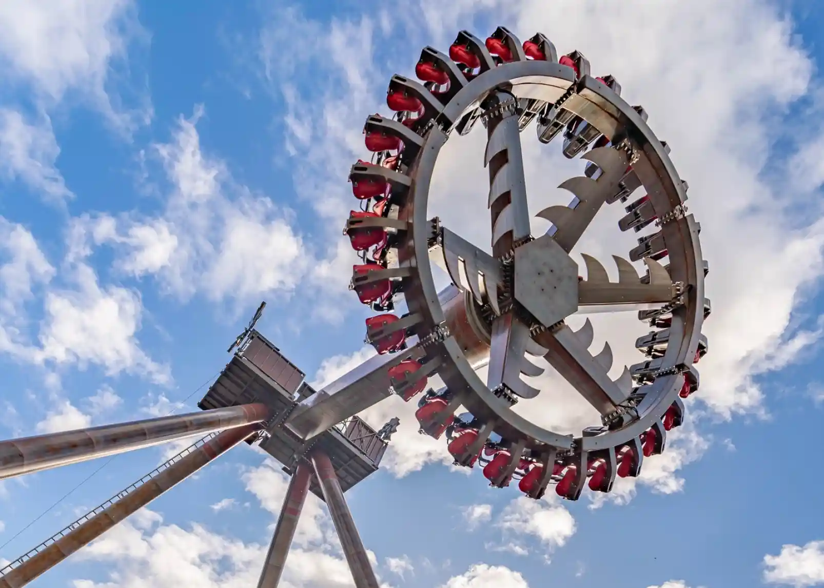 A roller coaster with vintage-style cars zooms through a loop under a clear blue sky. Riders are enjoying the thrill, with some raising their arms in excitement. The track is a bright yellow, contrasting with the surrounding landscape.