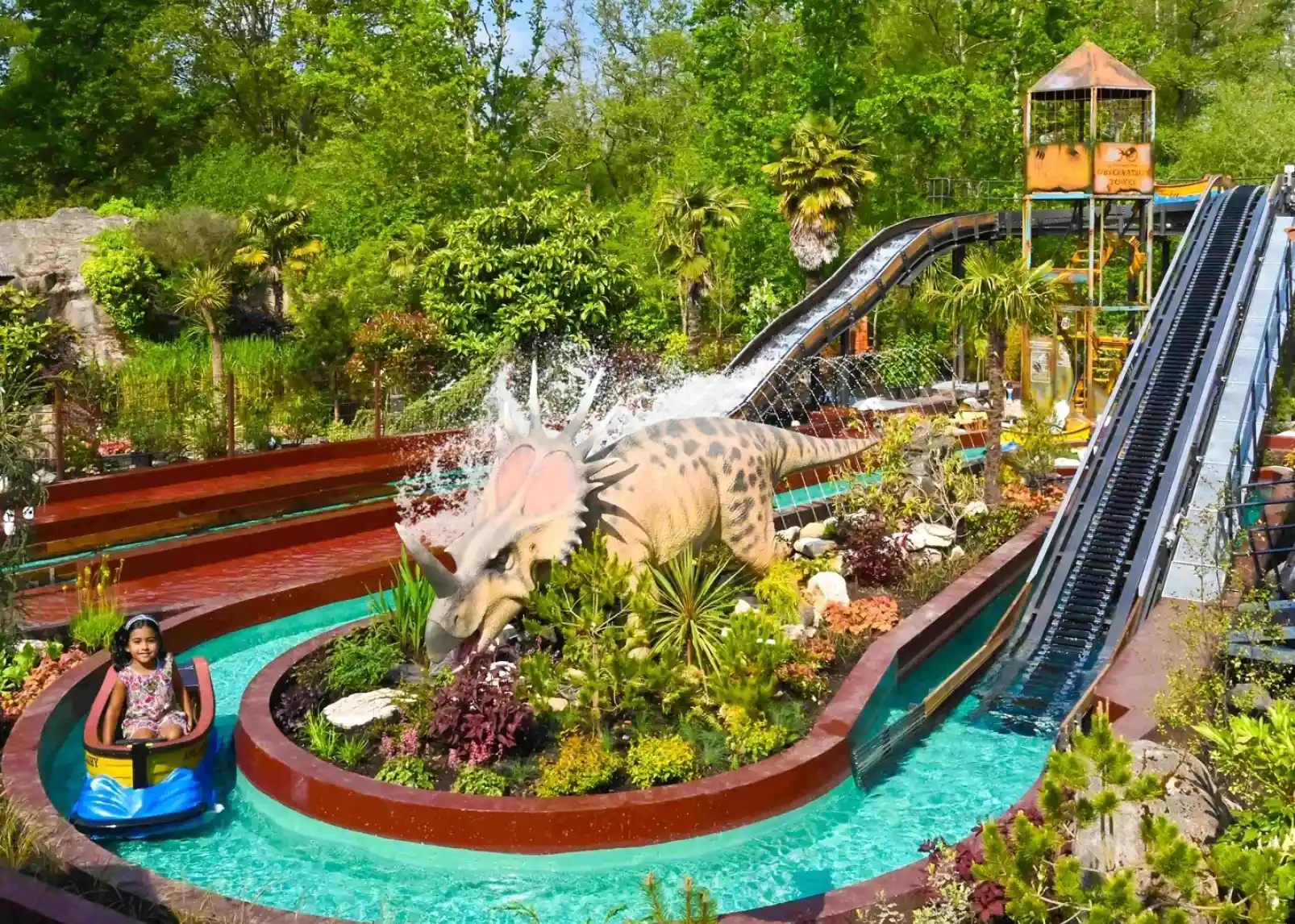 A roller coaster with vintage-style cars zooms through a loop under a clear blue sky. Riders are enjoying the thrill, with some raising their arms in excitement. The track is a bright yellow, contrasting with the surrounding landscape.