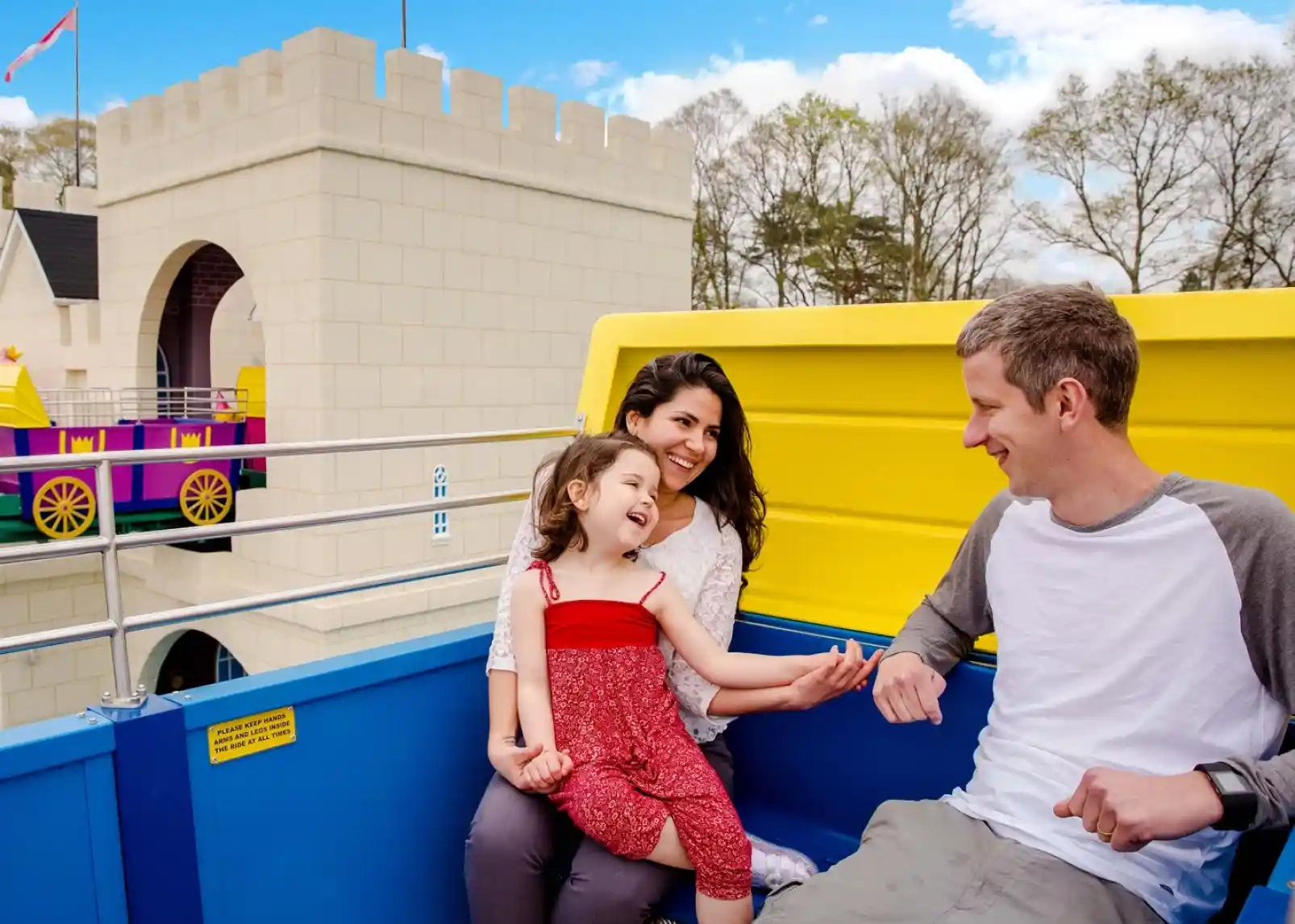 A group of animated characters from a children's show stands together, wearing colorful outfits. They are set against a backdrop of amusement park attractions, including colorful hot air balloons. The characters are smiling and appear cheerful.