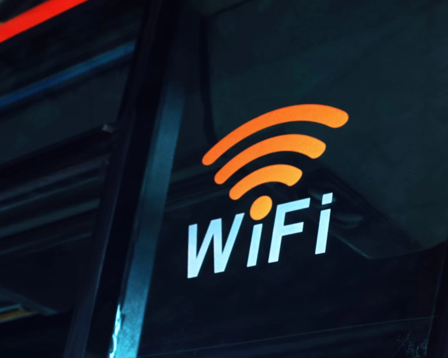 Orange WiFi symbol above the word 'WiFi' in white text, displayed on a glass window or door, indicating available wireless internet access.