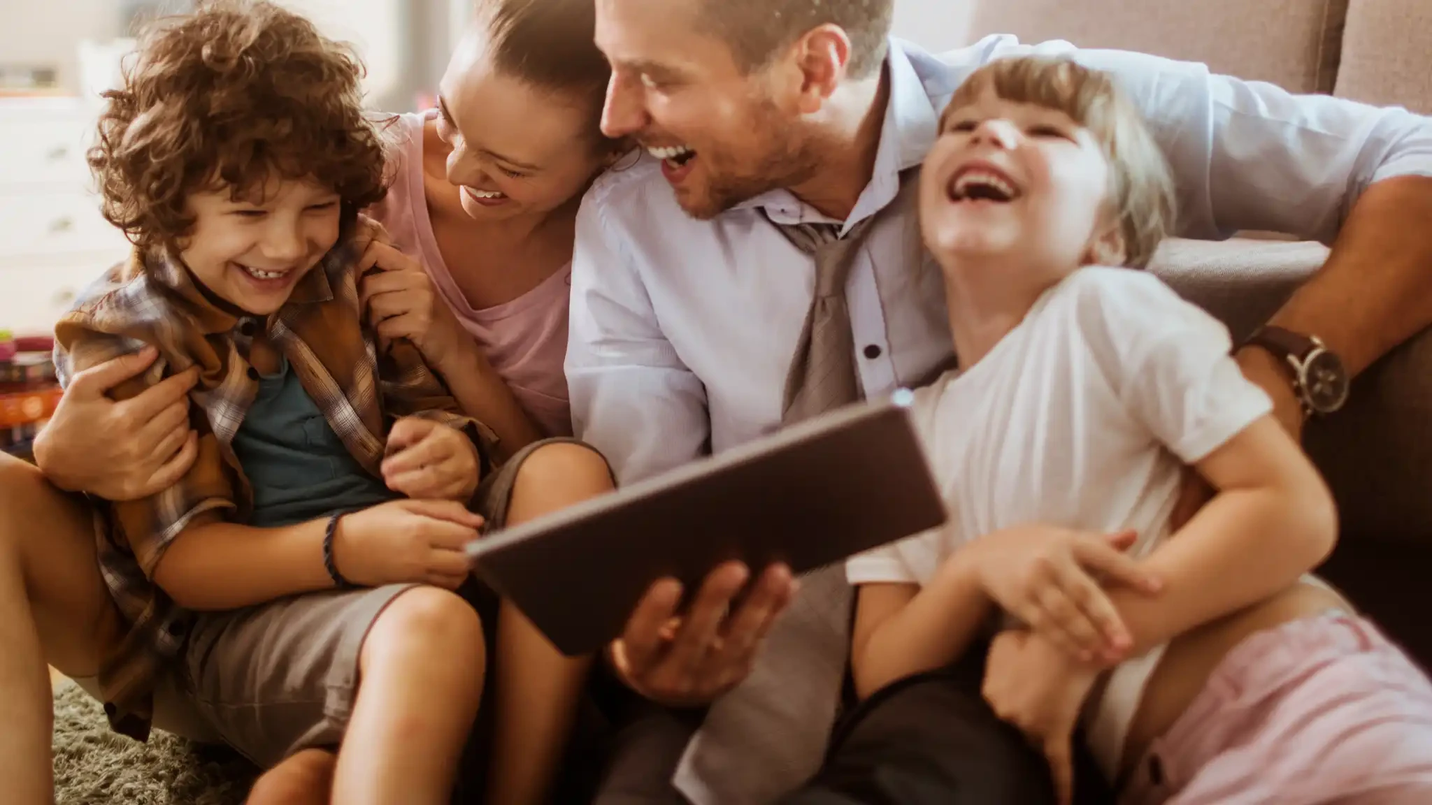 A happy family of four laughing while looking at a tablet.